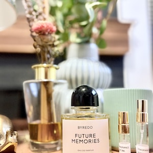 May include: A clear glass perfume bottle with a black cap and a white label reading BYREDO FUTURE MEMORIES EAU DE PARFUM, accompanied by two smaller clear glass sample vials with gold spray nozzles labeled FRAGRANCE EDP 3ML and 5ML.