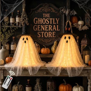 May include: Two illuminated ghost figures draped in sheer, white, star-patterned fabric, each wearing a black witch hat. The ghosts are positioned on a wooden shelf in front of a sign reading THE GHOSTLY GENERAL STORE, surrounded by pumpkins.
