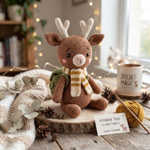 Peut inclure: Un jouet en crochet représentant un cerf marron avec des bois blancs, une écharpe rayée et un sac à dos vert. Une petite carte blanche devant indique Woodland Deer Crochet Pattern Instant Download. Une pelote de laine jaune et un crochet sont présents.