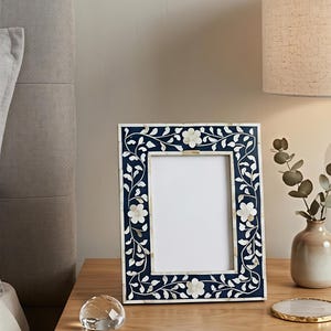 May include: A rectangular picture frame featuring a deep navy blue background with an intricate inlaid floral pattern in white. The design consists of delicate vines, leaves, and five-petaled flowers crafted from smooth, light-coloured material.