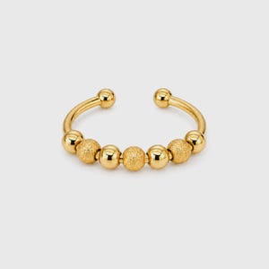 May include: A gold-colored open ring with a series of small, round beads. The ring features a smooth, polished finish on the band and the end beads, while the central beads have a textured, matte appearance. The ring is designed to be worn on a finger.