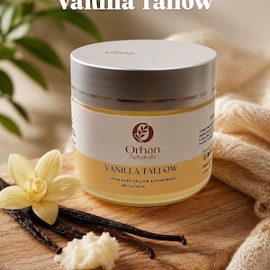 May include: A round jar of Orhan Naturals Vanilla Tallow with a silver lid. The label reads Vanilla Tallow, 100% Beef Tallow & Handmade, Net 2 oz | 60 ml. A pale yellow vanilla flower, dark vanilla beans, and a small scoop of white tallow sit nearby.