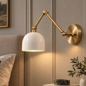 May include: A wall-mounted lamp featuring a white dome-shaped shade and an adjustable brass-toned metal arm. The fixture includes a circular brass wall plate and multiple pivot points, providing a functional lighting solution for a bedroom space.