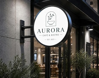 May include: A circular, illuminated outdoor sign mounted on a black metal bracket. The white sign features a black line drawing of a plant in a bowl, with the text AURORA CAFÉ & BISTRO and EST. 2023 printed in a clean, dark font.