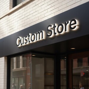 May include: Exterior shot of a storefront with a black sign that reads "Custom Store" in a bold, illuminated font. The sign is mounted on a dark panel above the glass entrance, set against a light-colored brick wall.