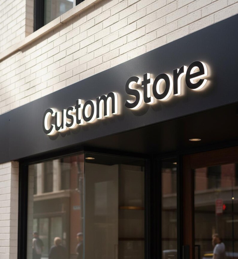 May include: Exterior shot of a storefront with a black sign that reads "Custom Store" in a bold, illuminated font. The sign is mounted on a dark panel above the glass entrance, set against a light-colored brick wall.