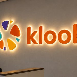 May include: A wall-mounted sign featuring the word klook in orange 3D letters alongside a circular logo composed of various orange, yellow, teal, and purple geometric shapes. The entire display is backlit, casting a soft glow against the wall.