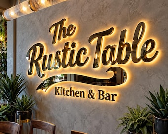 May include: A wall-mounted sign with gold-toned, reflective lettering that reads The Rustic Table Kitchen & Bar. The letters are backlit with a warm glow, mounted on a textured gray wall. Potted green plants are positioned below the sign.