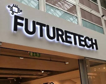 May include: A white storefront sign featuring the black text FUTURETECH in a bold sans-serif font, illuminated from behind with a white glow. To the left of the text is a black icon of a computer chip with four extending lines.