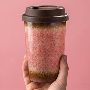 May include: A brown and pink travel mug with a matching lid. The mug has a textured, speckled appearance with a gradient of colors, transitioning from brown at the base to pink in the middle and brown at the top. The lid is closed.