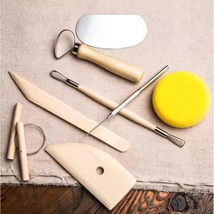 Peut inclure: Un ensemble d'outils de poterie, comprenant des outils de modelage en bois, une estèque en métal, une éponge et un coupe-fil. Les outils sont disposés sur une surface de couleur neutre, présentant la variété des formes et des fonctions pour le travail de la céramique.