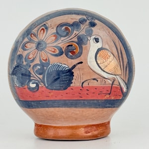 May include: Hand-painted ceramic vase with a bird and floral design. The vase features a white bird with orange and brown accents, set against a backdrop of flowers and foliage in blue, orange, and brown hues. A red stripe accents the base of the design.
