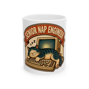 May include: A white ceramic mug featuring a graphic of a tabby cat sleeping on a vintage computer keyboard. Above the cat, a red banner displays the text SENIOR NAP ENGINEER in bold letters, with small black zzz symbols floating near the cat's head.