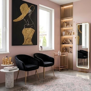 Op de afbeelding: Twee zwarte fluwelen stoelen met gouden poten in een kamer met roze muren, een marmeren bijzettafel met gouden flessen, een gouden rolwagen, een hoge verlichte spiegel en een groot zwart schilderij met een gouden glitter silhouet.