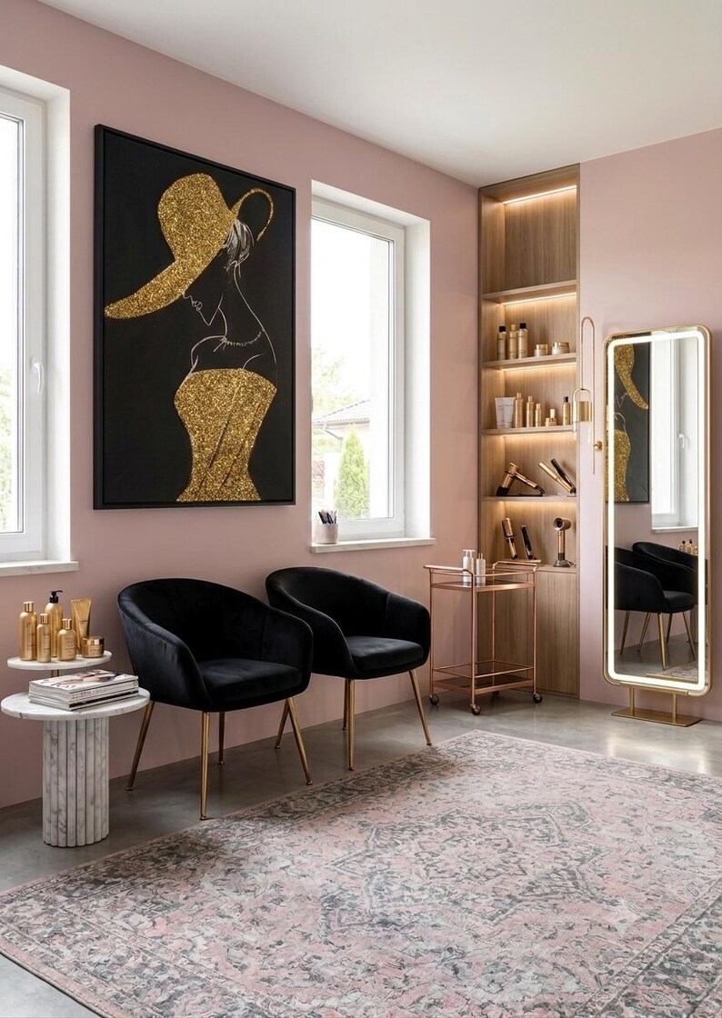 Op de afbeelding: Twee zwarte fluwelen stoelen met gouden poten in een kamer met roze muren, een marmeren bijzettafel met gouden flessen, een gouden rolwagen, een hoge verlichte spiegel en een groot zwart schilderij met een gouden glitter silhouet.