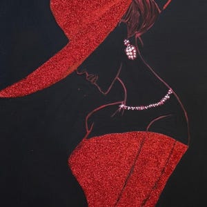 Op de afbeelding: Een wandkunstwerk met het silhouet van een figuur met een rode glitterhoed met brede rand en een bijpassende rode glitter strapless jurk. Het figuur is versierd met witte kralenoorbellen en een witte kralenketting tegen een zwarte achtergrond.