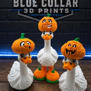 May include: Three white goose figurines with orange pumpkin hats. The center goose stands on two orange pumpkins, while the two side geese have pumpkins resting on their heads. Each pumpkin has a green stem and a unique carved facial expression.