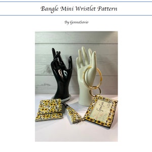 May include: A yellow and black wristlet with a sunflower pattern and a matching tassel. The wristlet has a clear plastic window with the text "Gemma Savio" inside. The wristlet is displayed on a white hand-shaped stand with a matching bangle.