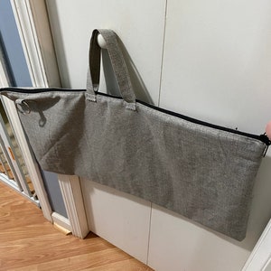 May include: A gray zippered storage bag with a black zipper and two black handles. The bag is hanging on a white door.
