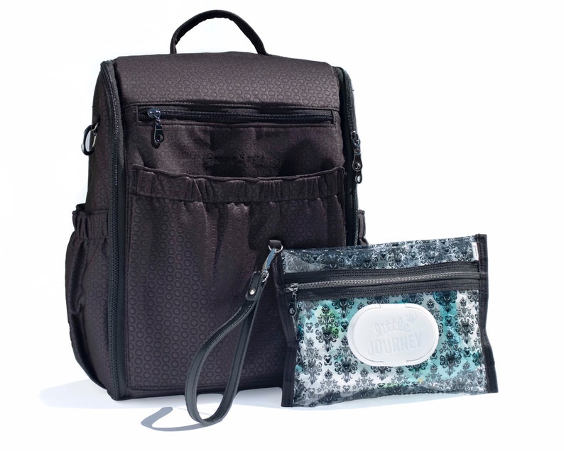 Puede incluir: Una mochila para pa&ntilde;ales negra con un patr&oacute;n geom&eacute;trico y m&uacute;ltiples bolsillos. Viene con una bolsa transparente con cremallera a juego con el texto "Little Journey" impreso en ella.