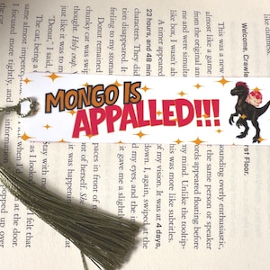 May include: A rectangular white bookmark featuring the orange text MONGO IS and large red text APPALED!!! with orange star accents. A black dinosaur illustration with a pink flower is on the right side. A metallic silver tassel is attached to the left.