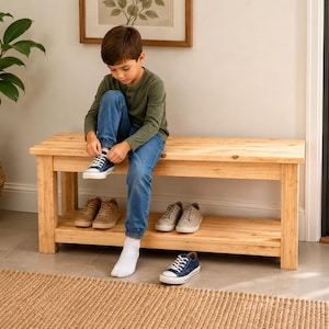 Peut inclure: Un banc rectangulaire en bois avec une finition naturelle à grain clair, quatre pieds robustes et une étagère de rangement inférieure. Le banc est conçu avec une surface supérieure plate et une étagère horizontale pour ranger les chaussures.