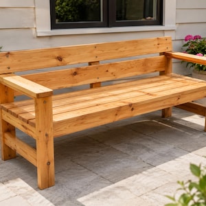 Könnte beinhalten: Holzbank mit natürlichem Finish. Die Bank hat eine Sitzfläche und Rückenlehne mit Lamellen sowie Armlehnen. Die Bank ist aus hellem Holz gefertigt und für den Außenbereich geeignet. Die Bank ist ca. 152 cm lang.