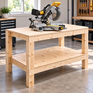 May include: A yellow and black miter saw sits on a rectangular wooden workbench with a lower shelf. The saw features a circular metal blade, a handle, and a base plate. The workbench is constructed from light-colored plywood boards.