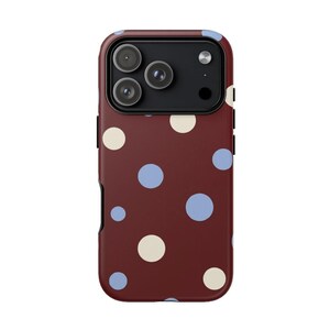 Könnte beinhalten: Eine weinrote Handyhülle mit einem Polka-Dot-Muster. Die Hülle hat ein sich wiederholendes Muster aus hellblauen und cremefarbenen Kreisen. Die Handyhülle hat einen Kameraausschnitt und einen schwarzen Rand.