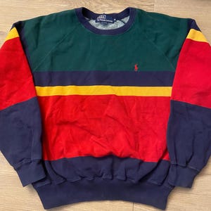 May include: A vintage crew neck sweatshirt with a color block design. The top section is green, with a yellow and navy blue stripe across the chest. The sleeves are red with navy blue cuffs. A small red polo logo is on the chest.