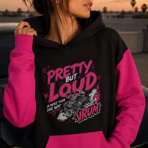 May include: Black hoodie with bright pink sleeves and a front pocket. The graphic on the front reads "Pretty But Loud" with a cartoon car engine and the word "Vrum".