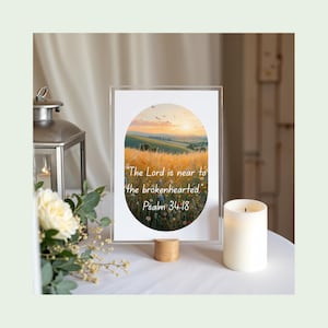May include: A rectangular acrylic sign with a wooden base featuring an oval print of a golden wheat field at sunset. The text reads, "The Lord is near to the brokenhearted." followed by "Psalm 34:18" in white lettering centered on the image.