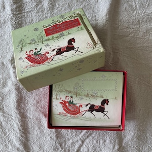 Peut inclure: Une boîte rectangulaire vert clair et un ensemble de cartes assorties représentant une scène hivernale avec un cheval noir tirant un traîneau rouge avec deux personnes. Le couvercle porte le texte Old Fashioned Christmas Selection.