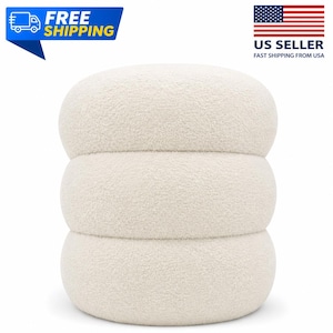 May include: A round, off-white ottoman featuring a textured, fuzzy fabric surface. The piece is constructed with three distinct, stacked, rounded segments that create a cylindrical shape with a soft, plush appearance and a uniform cream color.