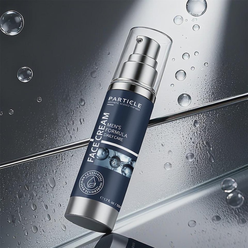 Op de afbeelding: Een zilveren en marineblauwe Particle gezichtscr&egrave;mefles met een doorzichtige pomptop. Het etiket leest "FACE CREAM", "MEN'S FORMULA DAILY CARE" en "1,7 fl oz / 50 ml". De achtergrond is een reflecterend oppervlak met waterdruppels.