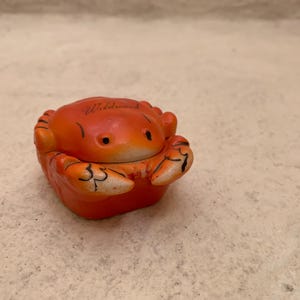 May include: Orange ceramic crab figurine with black eyes and the word "Wildwood" written on the top.