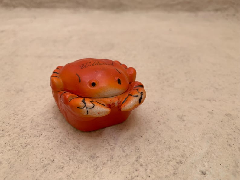 May include: Orange ceramic crab figurine with black eyes and the word "Wildwood" written on the top.