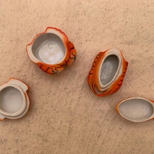 May include: Four small ceramic containers shaped like orange and white tigers. The containers are open and show the white ceramic interior.