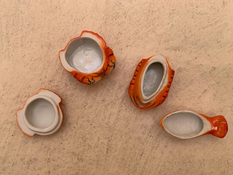 May include: Four small ceramic containers shaped like orange and white tigers. The containers are open and show the white ceramic interior.