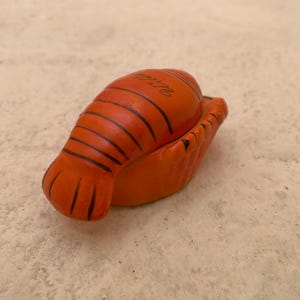 May include: Orange ceramic lobster shaped trinket box with black detailing. The box is closed and the top of the box has the text "Italia" written on it.