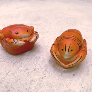 May include: Two ceramic figurines of a crab and a lobster. Both are orange with black details and have a glazed finish.