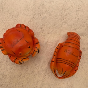 May include: Two orange ceramic figurines of a crab and a lobster. Both figurines have the word "Wildwood" written on them.