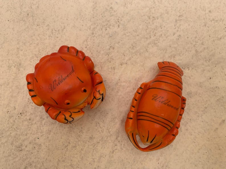 May include: Two orange ceramic figurines of a crab and a lobster. Both figurines have the word "Wildwood" written on them.