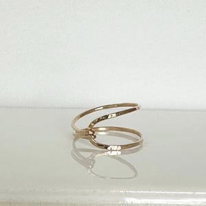 May include: A gold ring with a simple, minimalist design. The ring is made of two thin bands of metal that are intertwined.