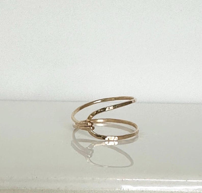 May include: A gold ring with a simple, minimalist design. The ring is made of two thin bands of metal that are intertwined.