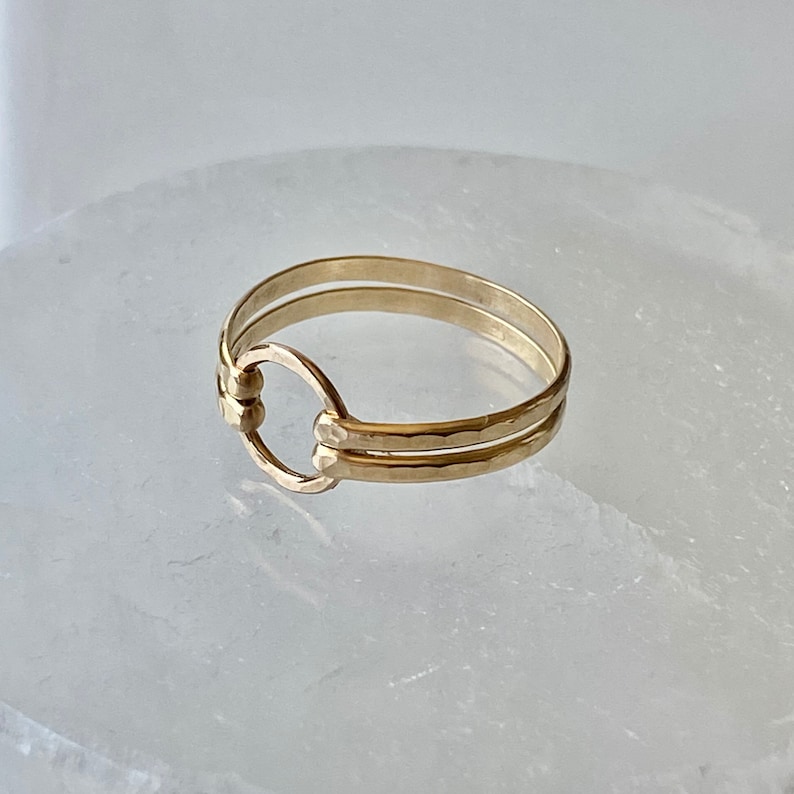 May include: A gold ring with a hammered finish and a circle design. The ring is double-banded.