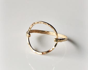 May include: A gold hammered circle ring with a smooth, polished finish. The ring is open in the center, creating a minimalist and modern design.