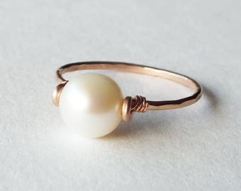 May include: A simple rose gold ring with a single white pearl wrapped in wire.