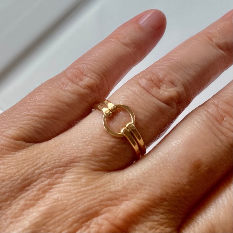 May include: A gold ring with a circle design. The ring is worn on a finger.