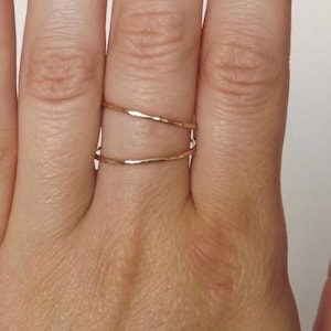 May include: Two thin gold rings on a finger. The rings are hammered and have a slightly irregular shape.
